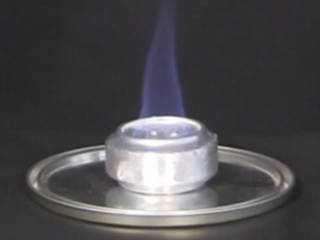 An alocohol stove made from soda cans with a flame burning from its wick.
