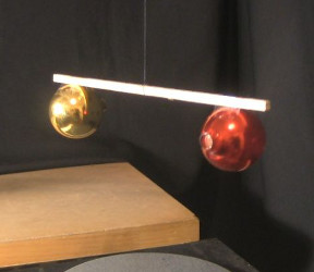 Christmas tree ornaments attached to either end of a bar with their holes facing opposite directions and with the bar suspended by a thread with a fishing spinner.