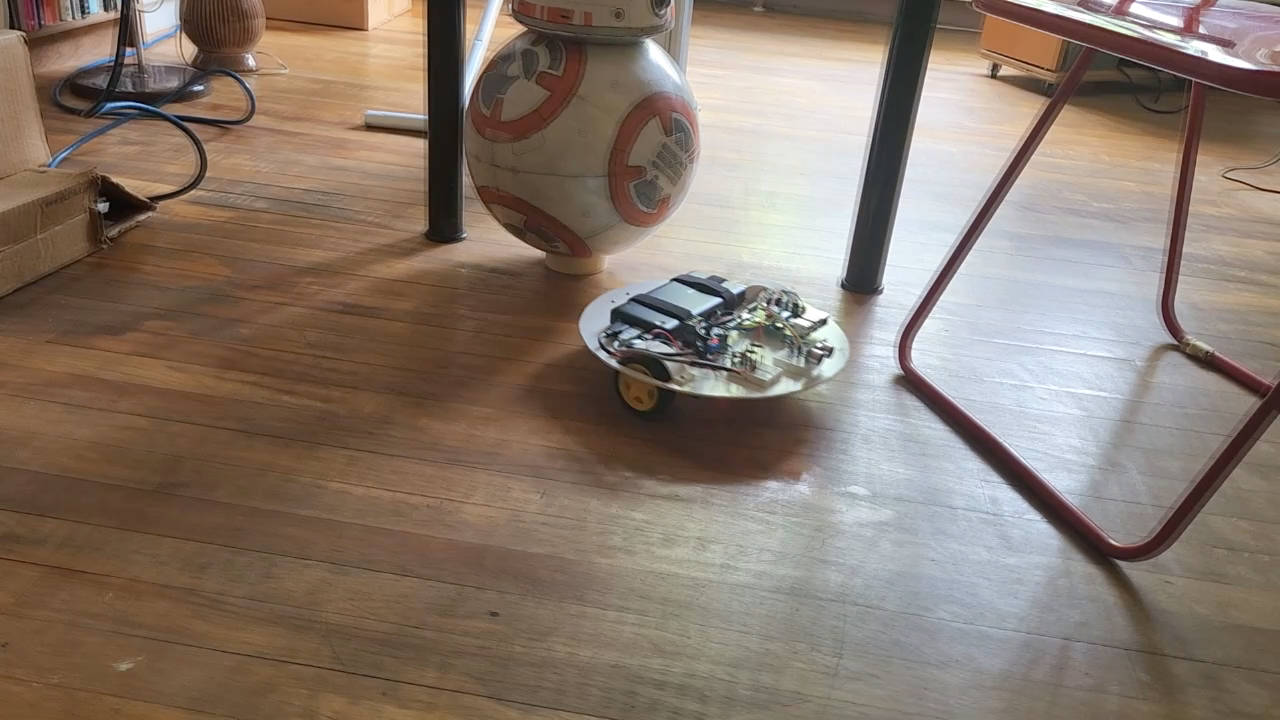 3-wheeled robot roaming around, avoiding obstacles, a BB-8 droid and a chair.