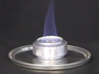 An alocohol stove made from soda cans with a flame burning from its wick.